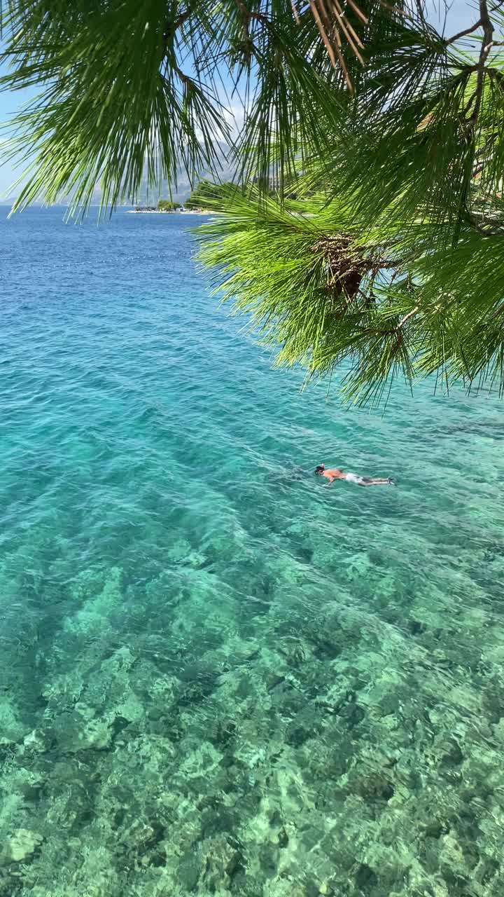 一名年轻人戴着潜水面罩在碧绿的水中游泳。视频素材