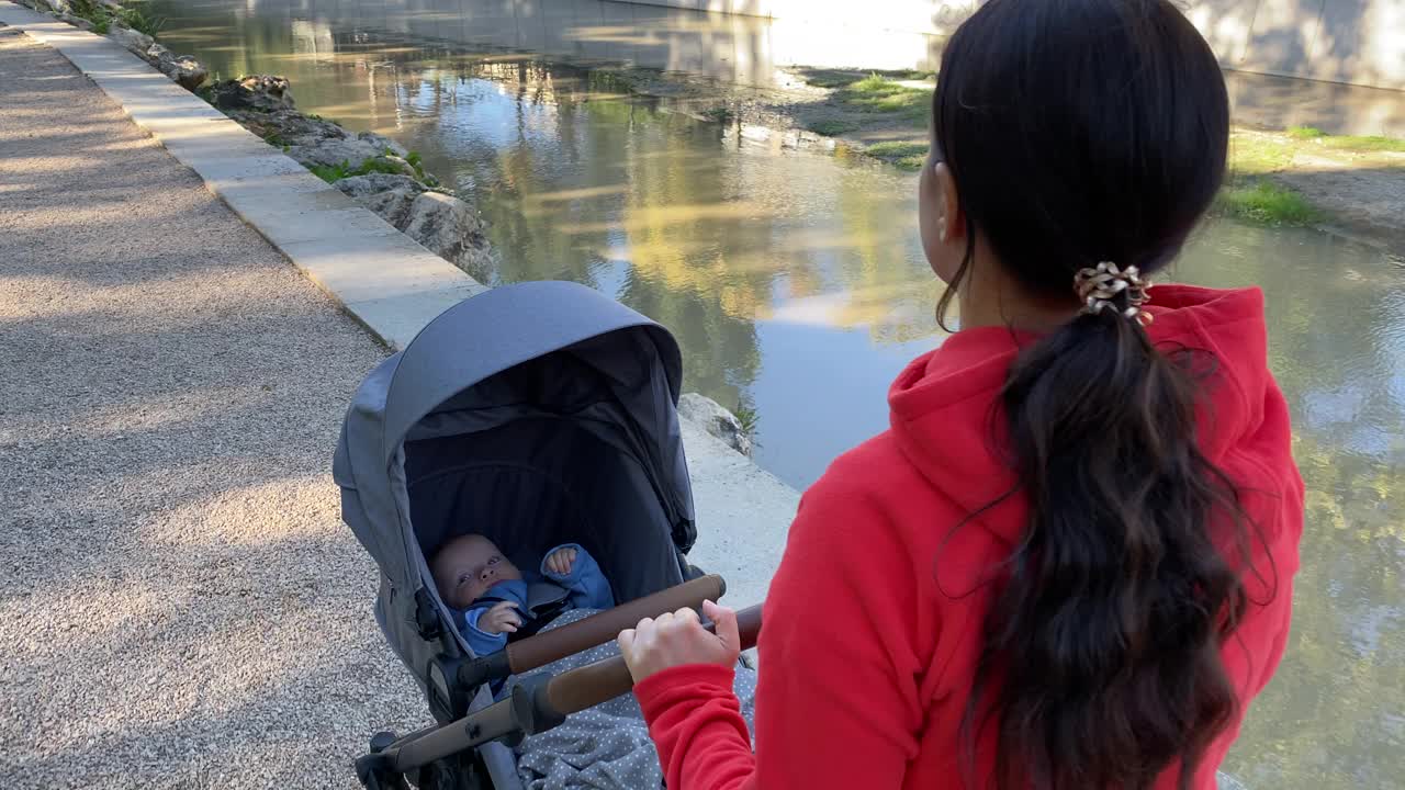 一个阳光明媚的夏日，妈妈推着婴儿车在公园小路上散步。视频素材