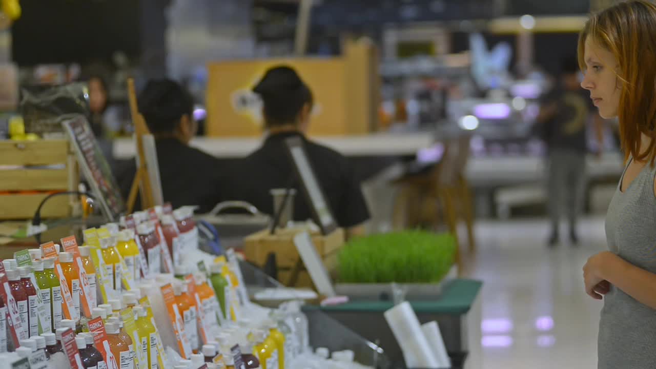 年轻女子在健康食品超市选择瓶装有机饮料视频素材