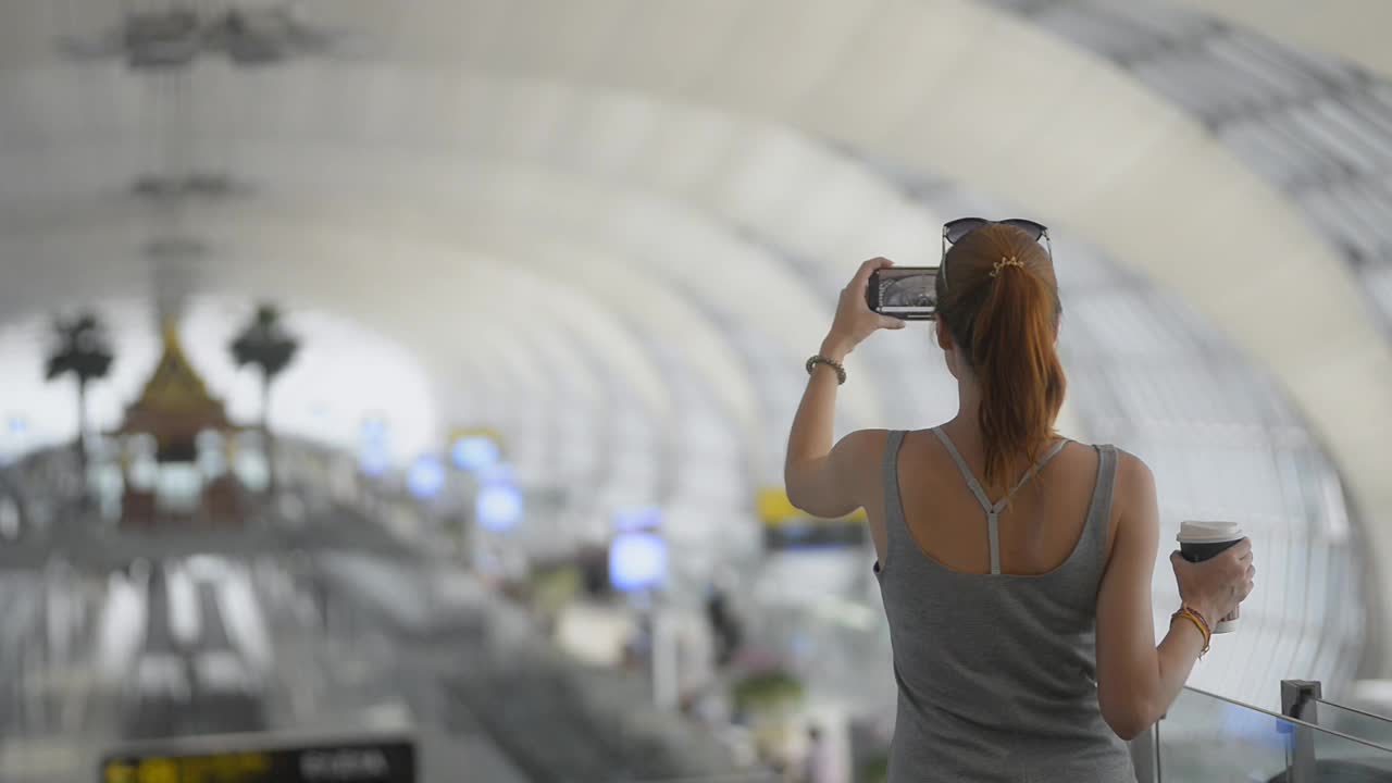 一名白人女旅客在机场拍照。手持手机在终端等待视频素材