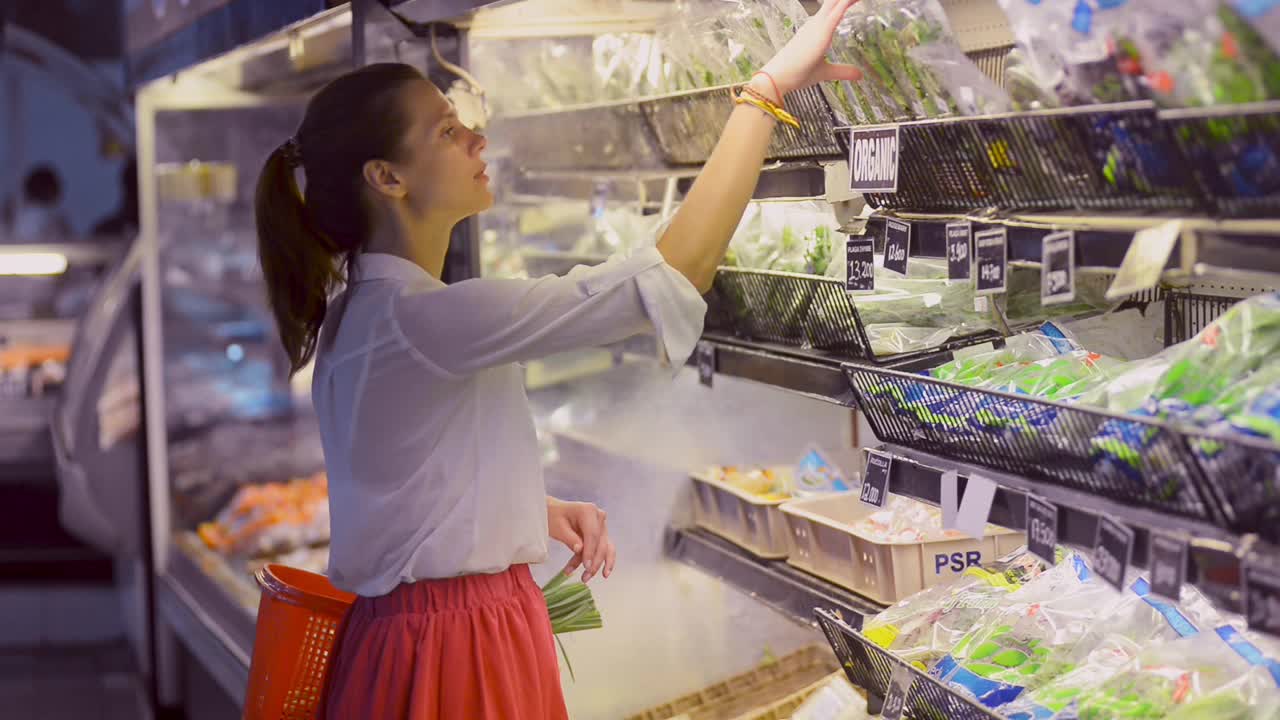 一名年轻的素食女子站在有机商店里，闻着绿色蔬菜，然后选择了绿色蔬菜视频素材