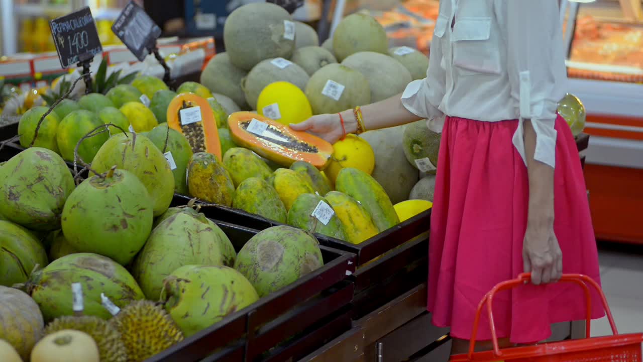 年轻的美国女人在亚洲旅行期间站在超市里挑选异国水果视频素材