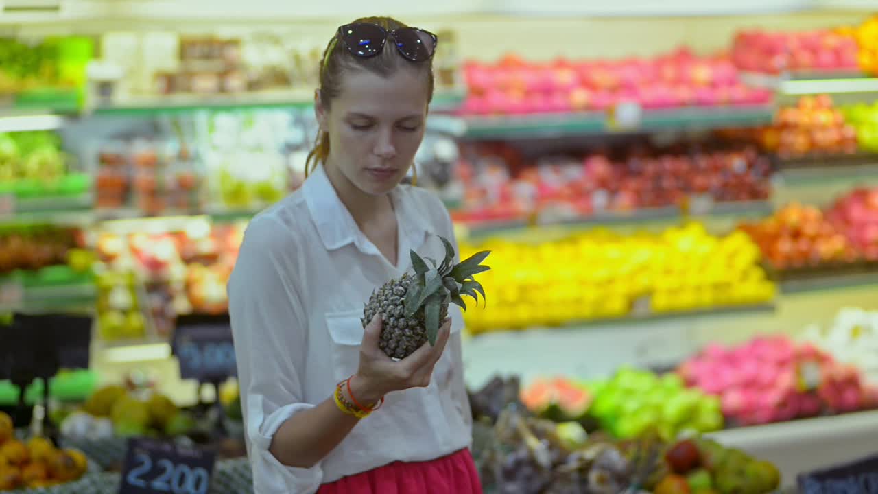 年轻女子旅行者在亚洲超市挑选异国情调的菠萝。美国女性选择视频素材