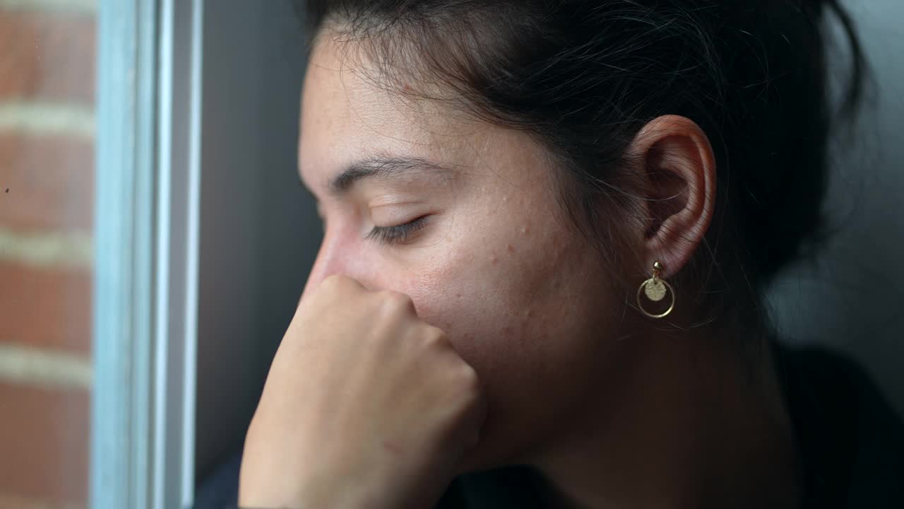 一个沉思的女人坐在窗边看着外面。特写镜头有思想的人视频素材