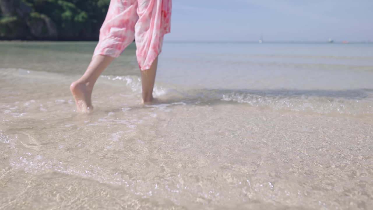 低角度的身体部分的女性行走在岛水海滩的波浪。漂亮姑娘和浪花海浪，暑假慢镜头。逃离繁忙污染的城市生活，旅游目的地视频素材