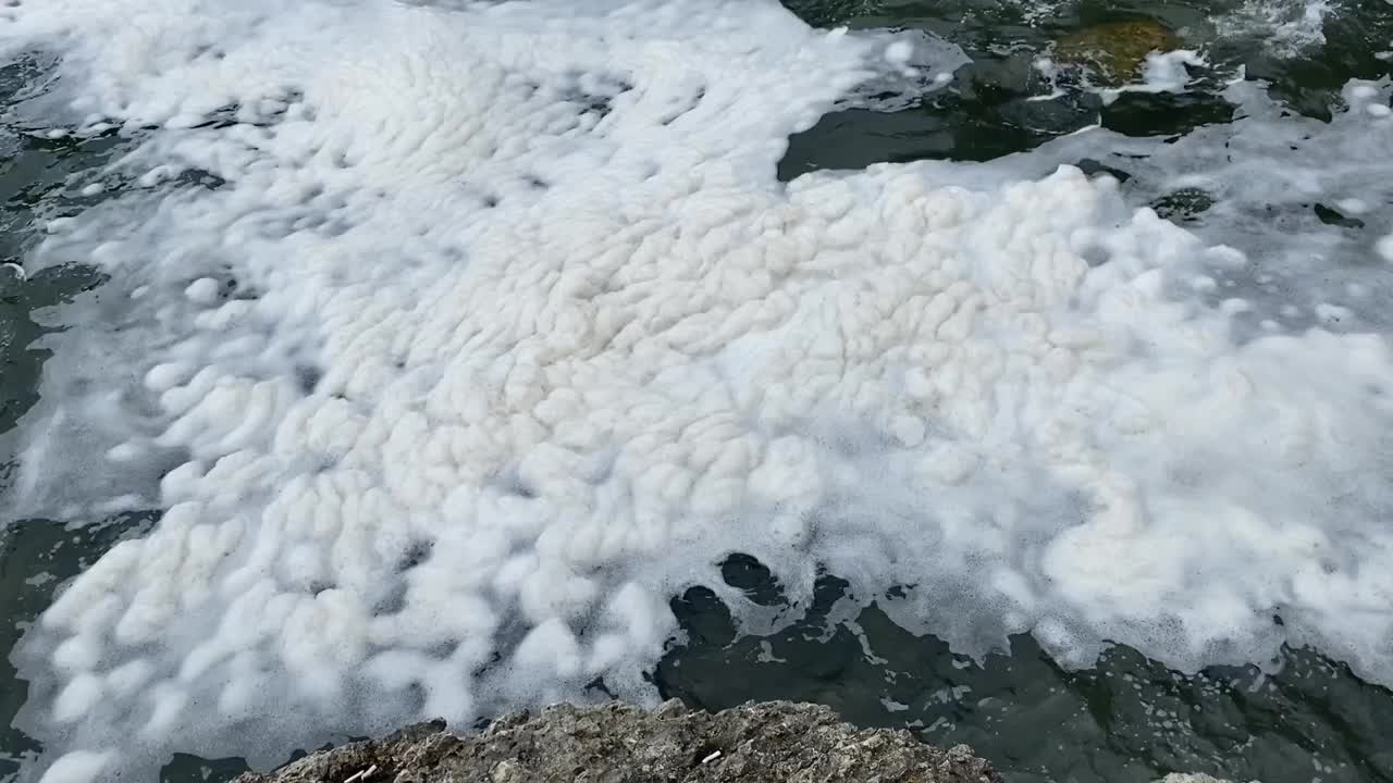 海面上的厚泡沫是海盐、藻类和各种废弃物的巨大堆积，在风和强海流的影响下，被吹成泡沫冲上岸。波涛汹涌的海面上，厚厚的泡沫被风吹散。视频素材