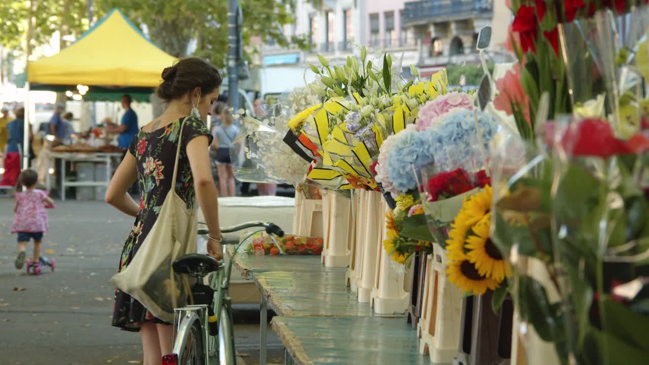 在法国布兰托姆，一名年轻女子在街市摊位上买花视频素材