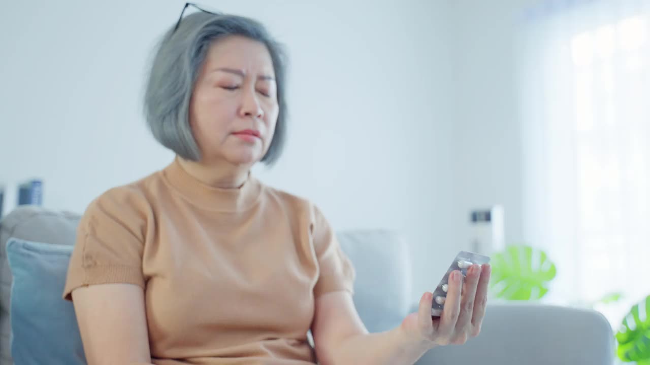 亚洲老年妇女病人坐在轮椅上在养老院护理。成熟的老年残疾女性看药瓶和阅读处方和内容在手。医疗保险的概念。视频素材