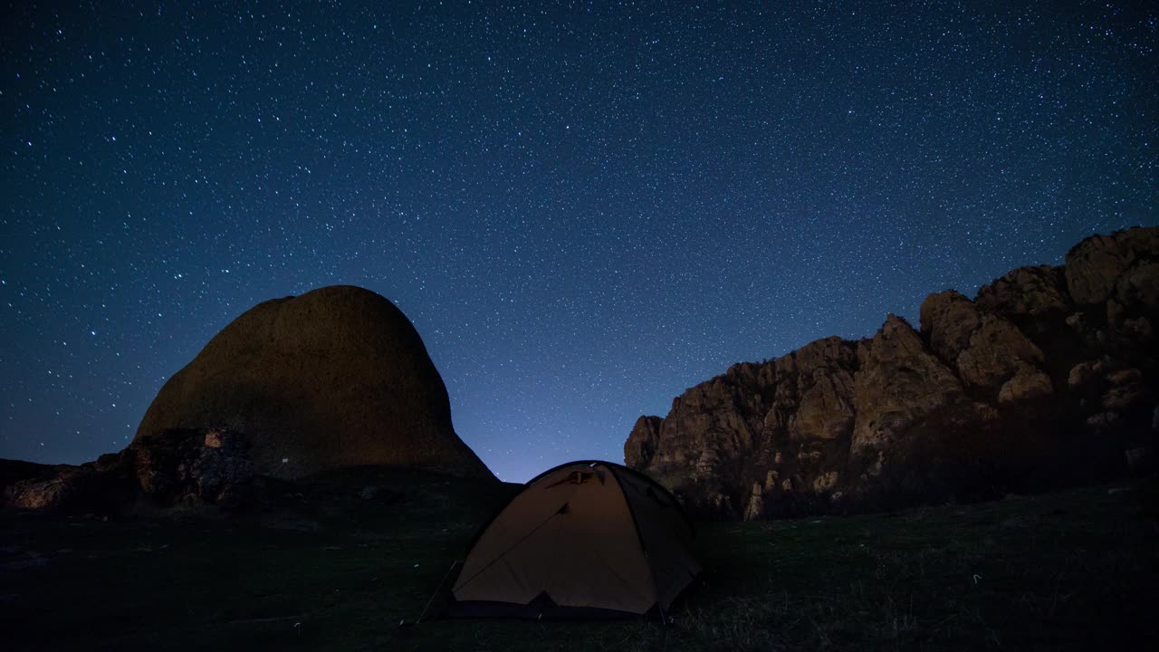 延时。星星在夜山和发光的露营帐篷上空盘旋视频素材