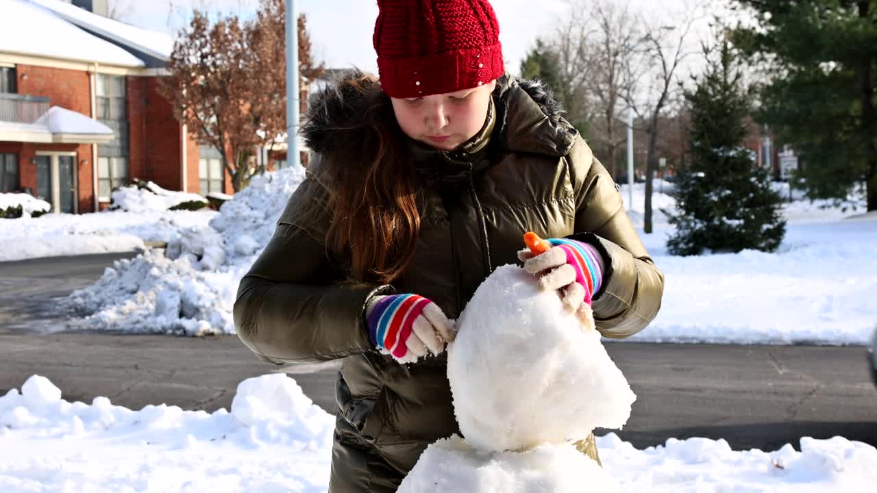 圣诞季节快乐的小女孩玩雪人在下雪的冬天一个十几岁的女孩雕刻雪人视频素材