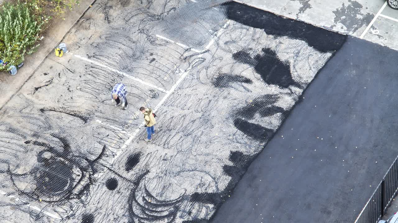 一组工人在停车场铺沥青的镜头。小压倒对方。道路施工工人穿着防护服，拿着铁锹。空中,俯视图视频下载