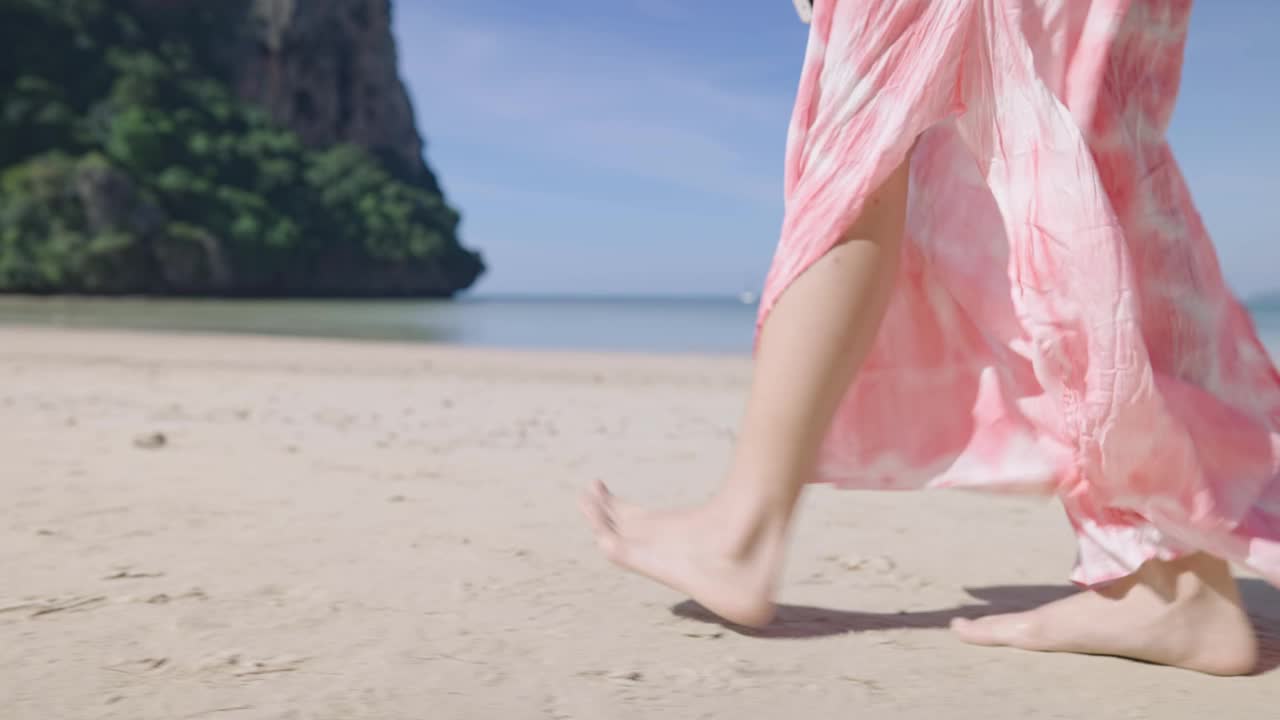 年轻美丽的女士走在有风的海滩上，风吹着衣服慢动作。度假旅游目的地人间天堂，悠闲漫步沙滩风光。夏装沙滩服视频素材