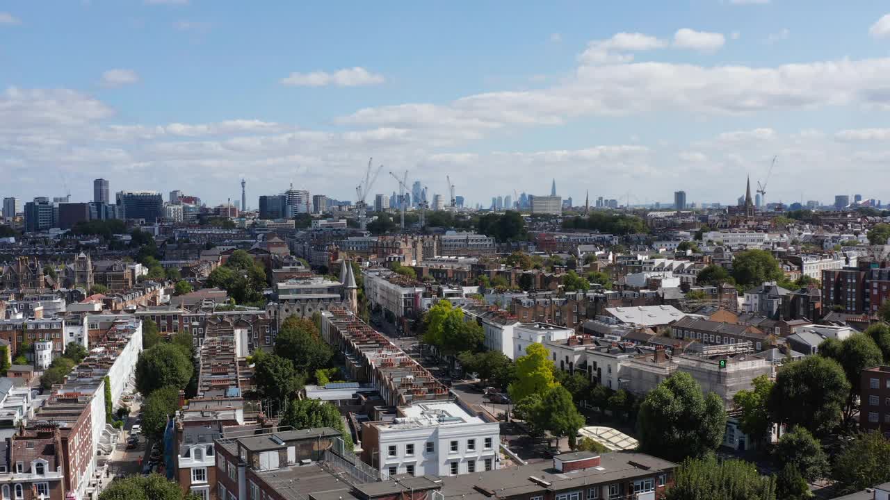 在住宅区的街道和联排别墅上空缓慢飞行。城市景观与高高的现代摩天大楼在远处。英国伦敦视频素材