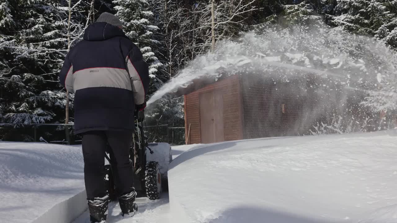 有人用吹雪机清扫人行道上的积雪。暴风雪过后，冬日阳光明媚的乡间小屋。视频素材