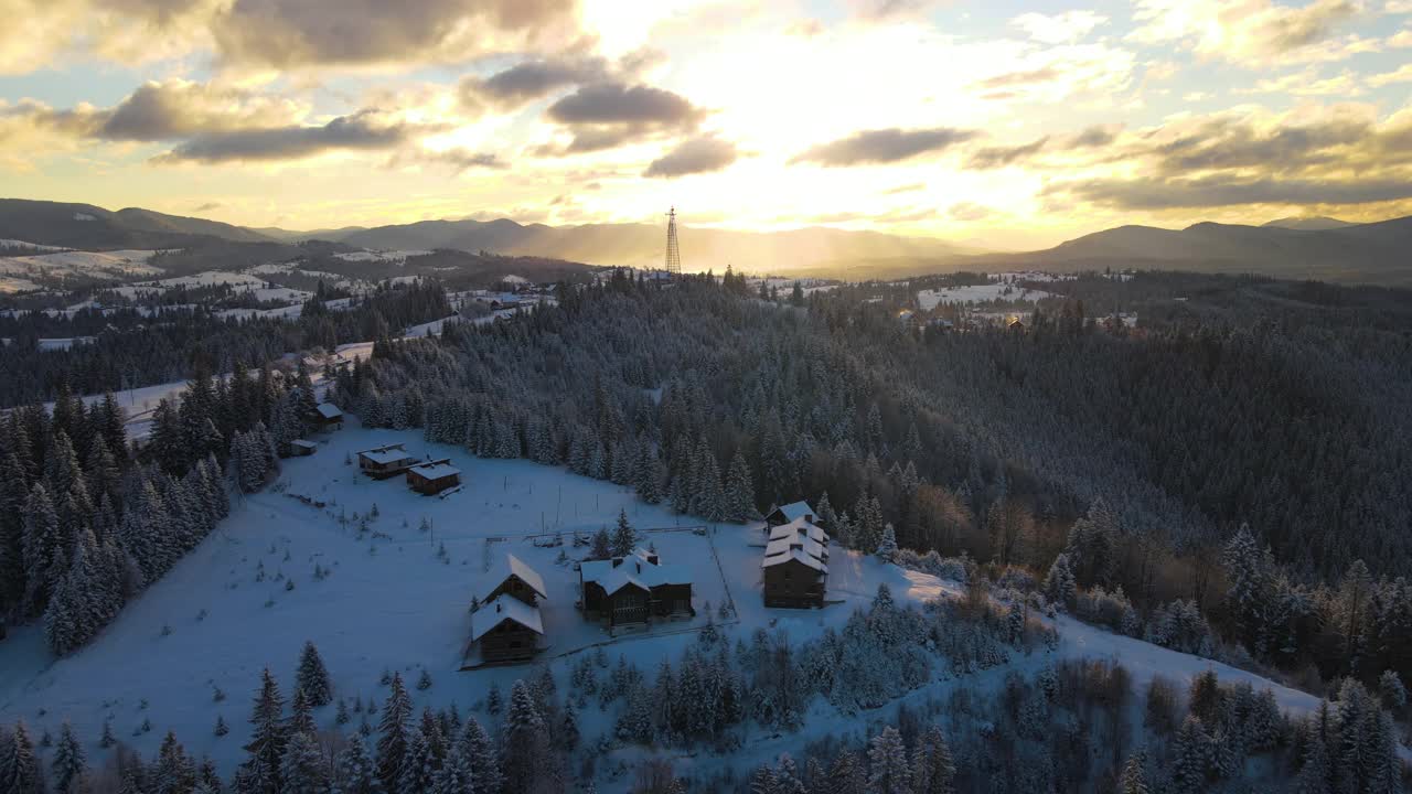 空中冬季景观与小村庄房屋之间的雪覆盖森林在寒冷的山在晚上。视频素材