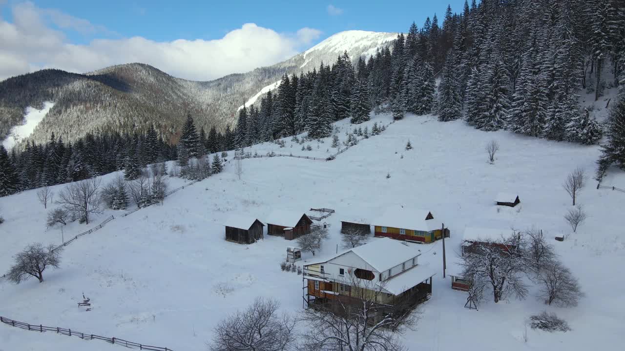 空中冬季景观与小乡村房屋之间的雪覆盖森林在寒冷的山。视频素材