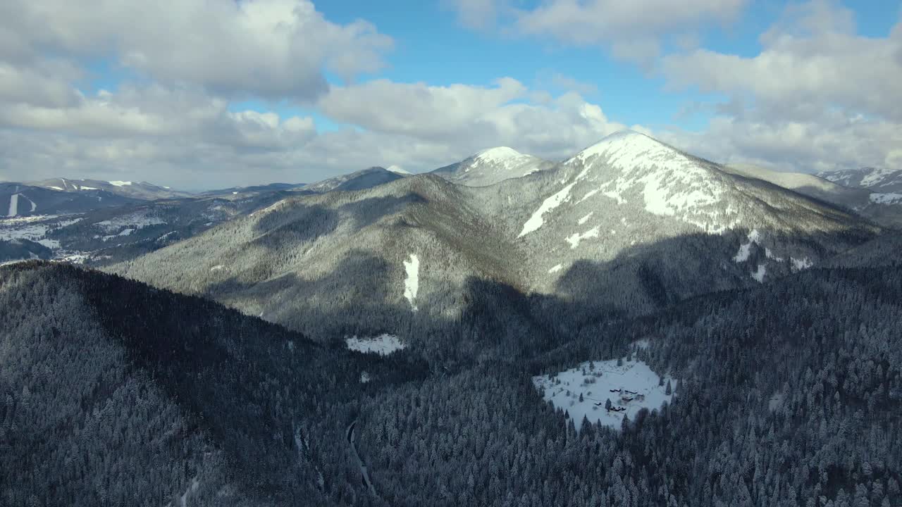 空中冬季景观与小乡村房屋之间的雪覆盖森林在寒冷的山。视频素材