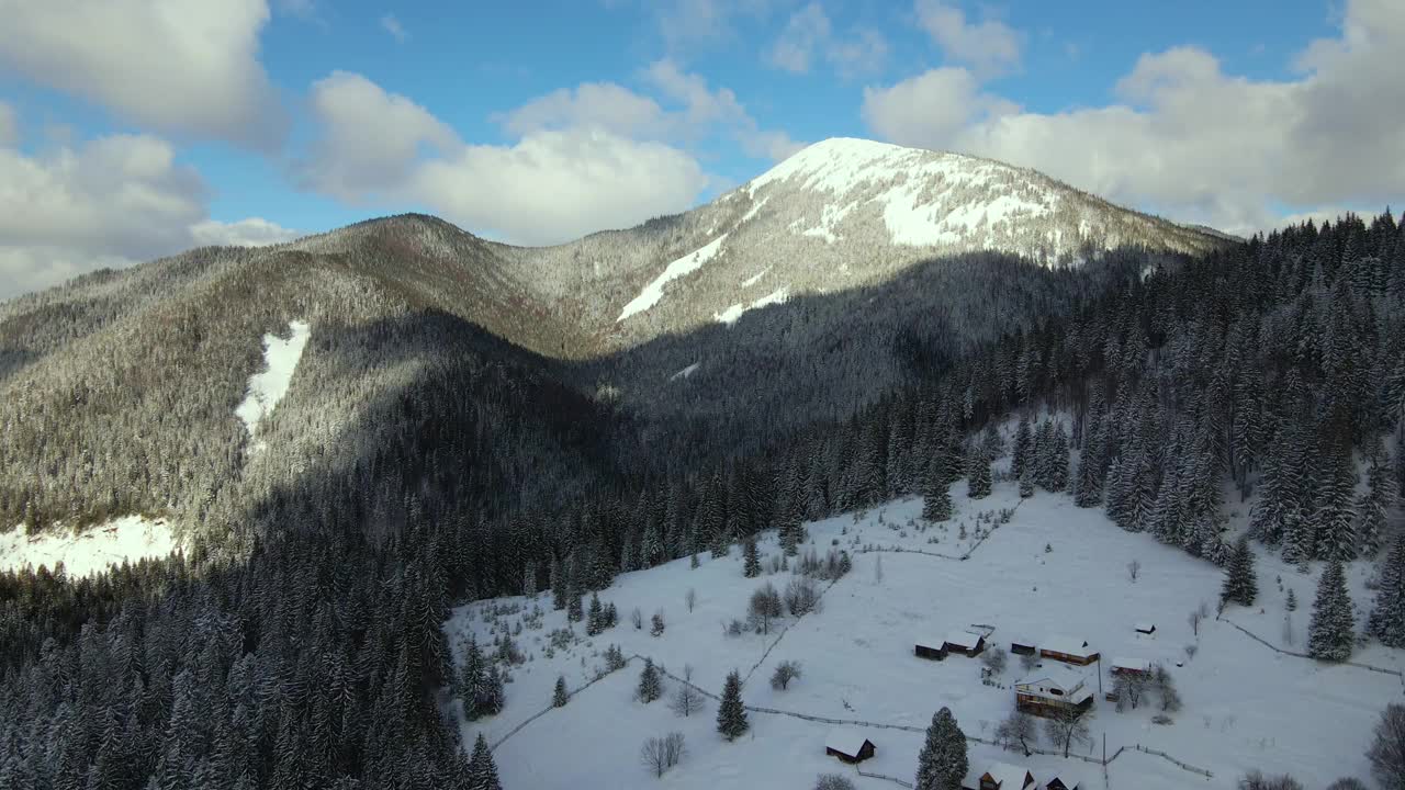 空中冬季景观与小乡村房屋之间的雪覆盖森林在寒冷的山。视频素材