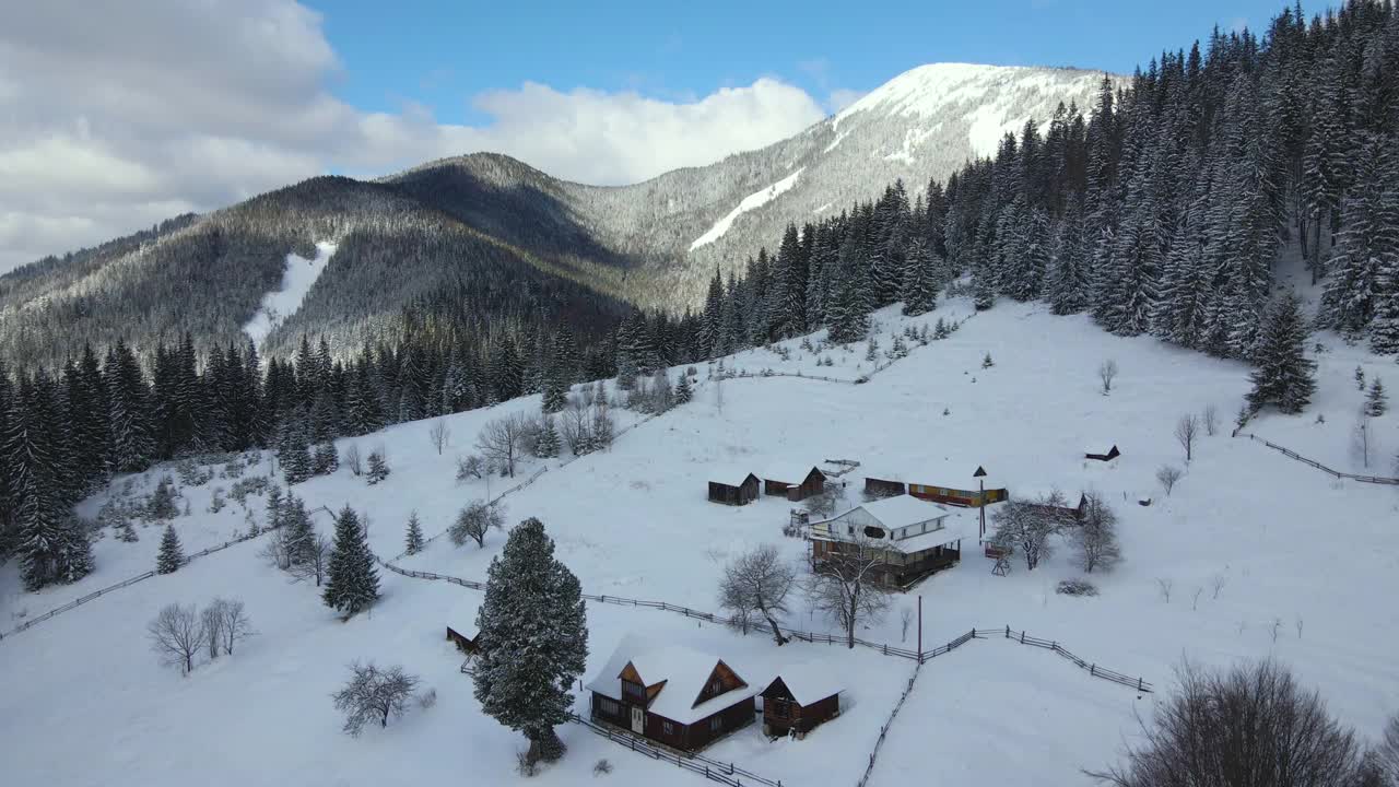 空中冬季景观与小乡村房屋之间的雪覆盖森林在寒冷的山。视频素材