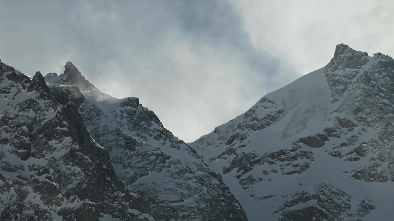 在长焦镜头上的时间流逝，高山的雪峰被风吹起的雪。山区恶劣的天气条件视频素材