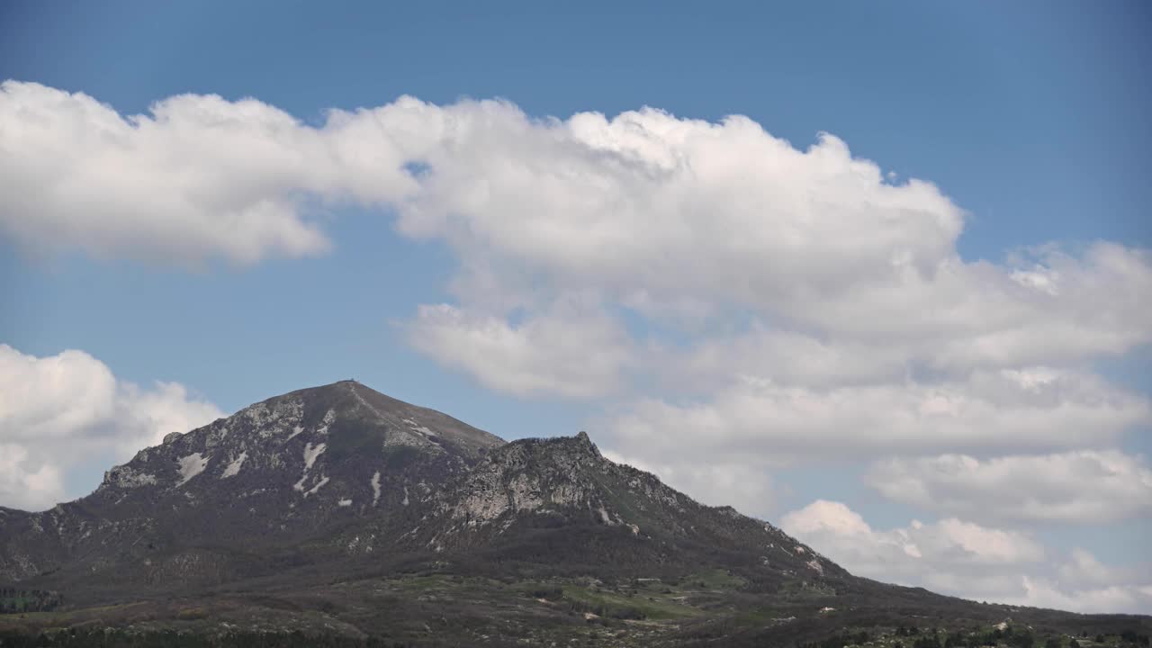 夏日的白天，在一座有几座山峰的山上，云朵飘浮，在绿色的森林里投下阴影。视频素材