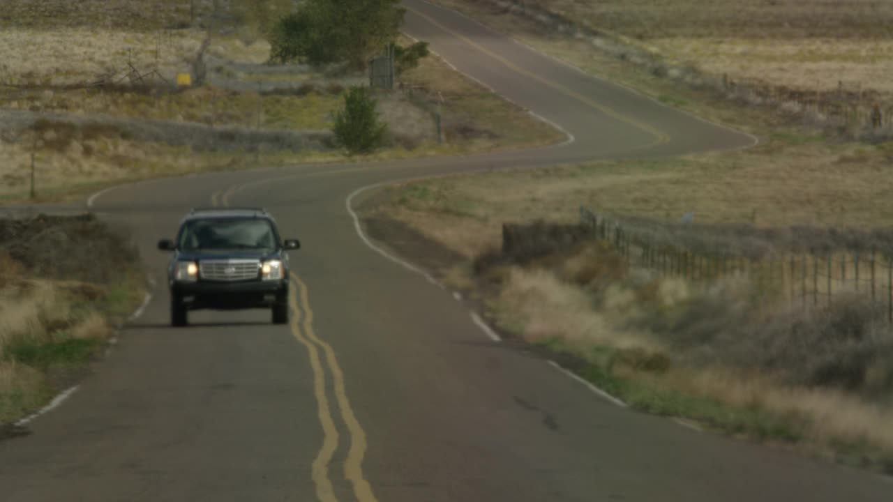 广角的农村地区或乡村道路。可见的干灌木或草。可能是沙漠公路。越野车朝摄像机开过去。可见的热量从道路上闪烁。视频素材