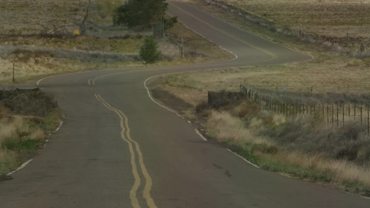 广角的农村地区或乡村道路。可见的干灌木或草。可能是沙漠公路。汽车或越野车部分可见，在镜头的最后走向相机。可见的热量从道路上闪烁。视频素材