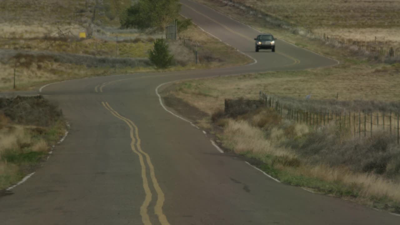 广角的农村地区或乡村道路。可见的干灌木或草。可能是沙漠公路。越野车朝摄像机开过去。可见的热量从道路上闪烁。视频素材