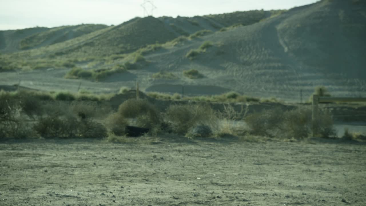 中等角度的土块或废弃的土地在农村或沙漠。在bg中可见的山脉或小山。灌木、橡胶轮胎和部分木栅栏可见。视频素材