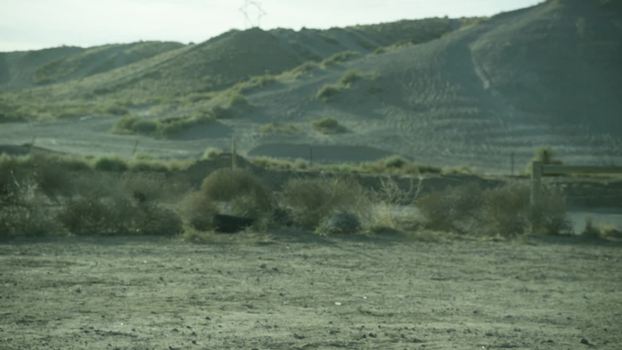 中等角度的土块或废弃的土地在农村或沙漠。在bg中可见的山脉或小山。灌木、橡胶轮胎和部分木栅栏可见。视频素材