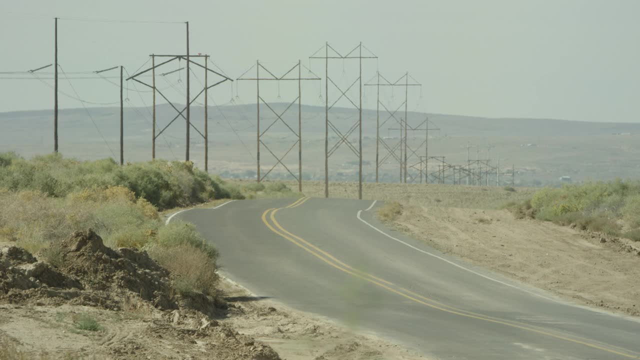 广角的乡村公路或沙漠公路。电力线、山脉或小山和灌木丛随处可见。可能是农村地区。视频素材