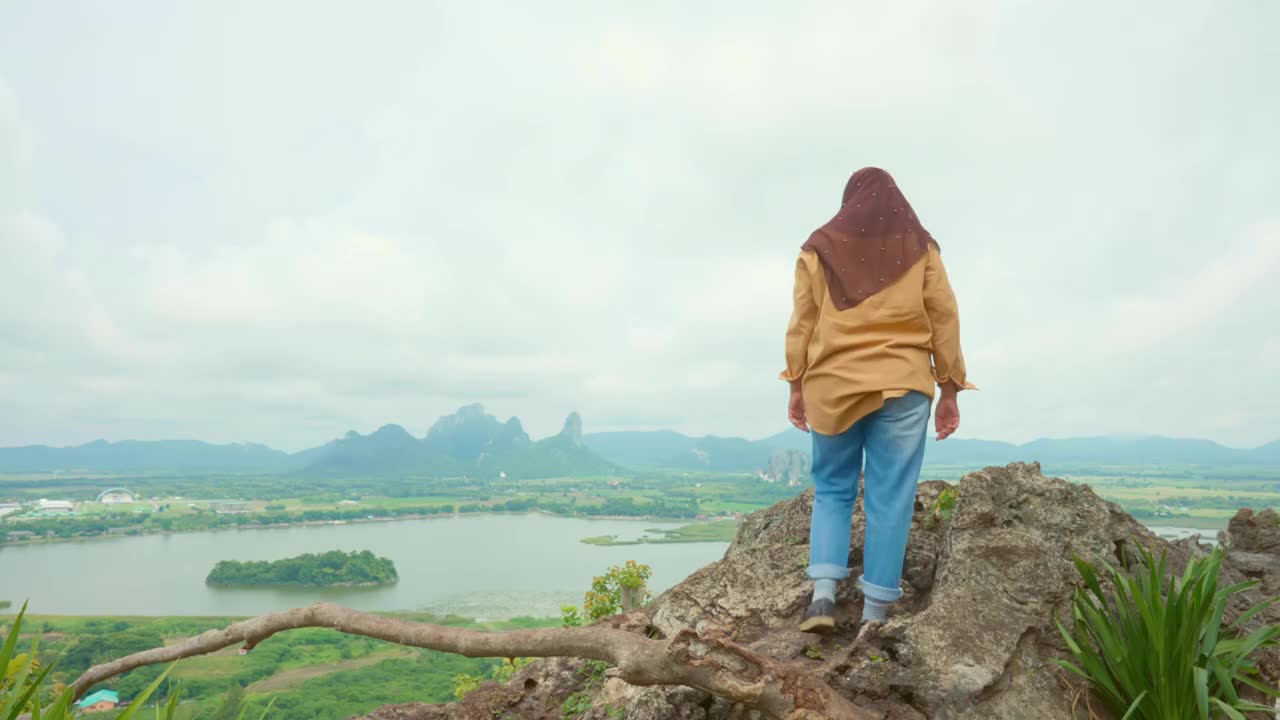 美丽健康的亚洲穆斯林妇女徒步上山，欣赏泰国岛的景色，享受自然景观的宁静和山丘和树木的背景视频素材