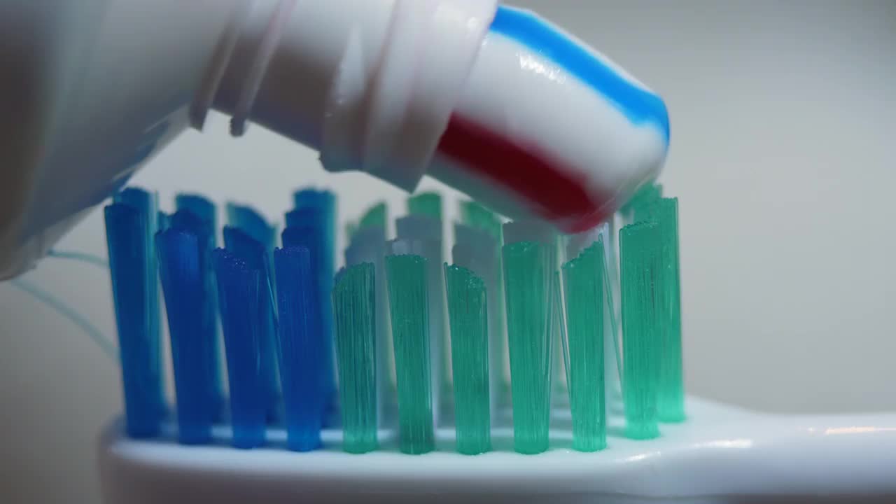带有亮条纹牙膏的牙刷特写。微距拍摄红色和蓝色条纹牙膏挤在牙刷上特写。牙科保健或口腔卫生。早上刷牙。视频素材