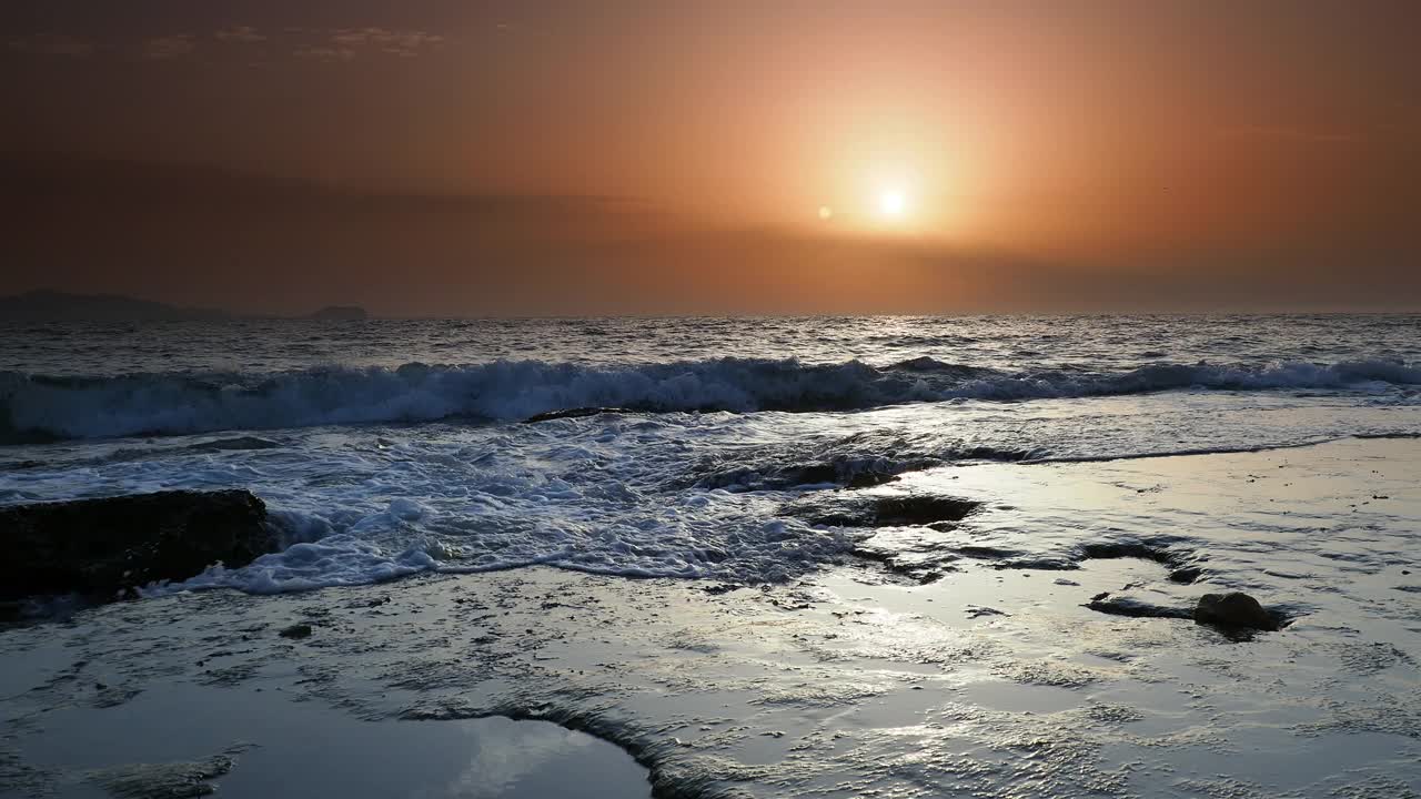 日出时的海岸线景观，太阳在地平线上，海浪拍打着海岸。视频素材