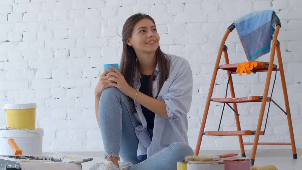 年轻的白种女人在装修房子。一名女画家在一间公寓的墙上休息。家居概念。新屋的概念。4 k慢动作视频素材