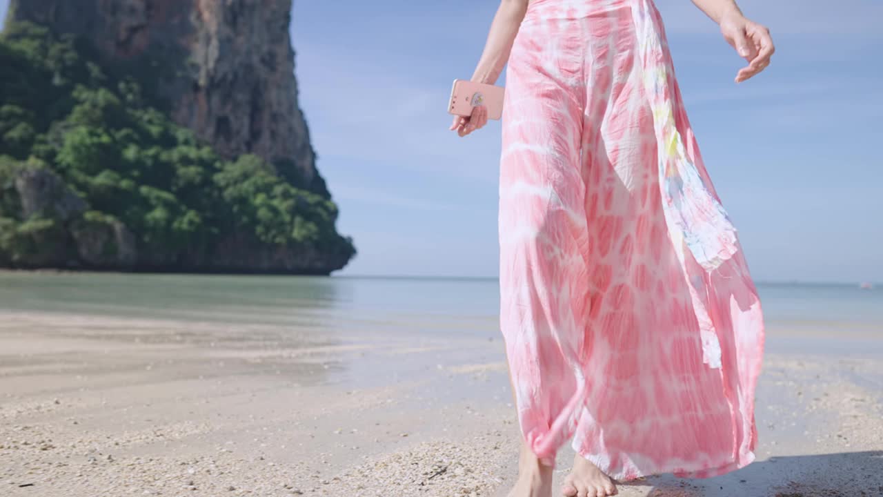 自信的女人走在沙滩上，亚洲热带岛屿慢动作。有风的流动海岸，悬崖山海岸的背景快乐放松海滩散步的场景。夏季时尚，亚洲旅行视频素材