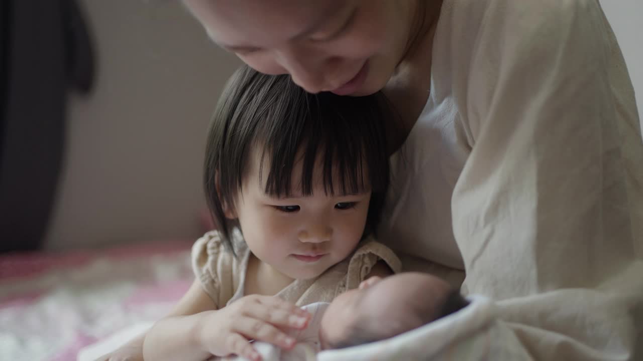 妈妈和妹妹在家里的卧室里照顾婴儿。视频素材