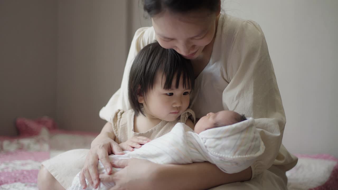 妈妈和妹妹在家里的卧室里照顾婴儿。视频素材