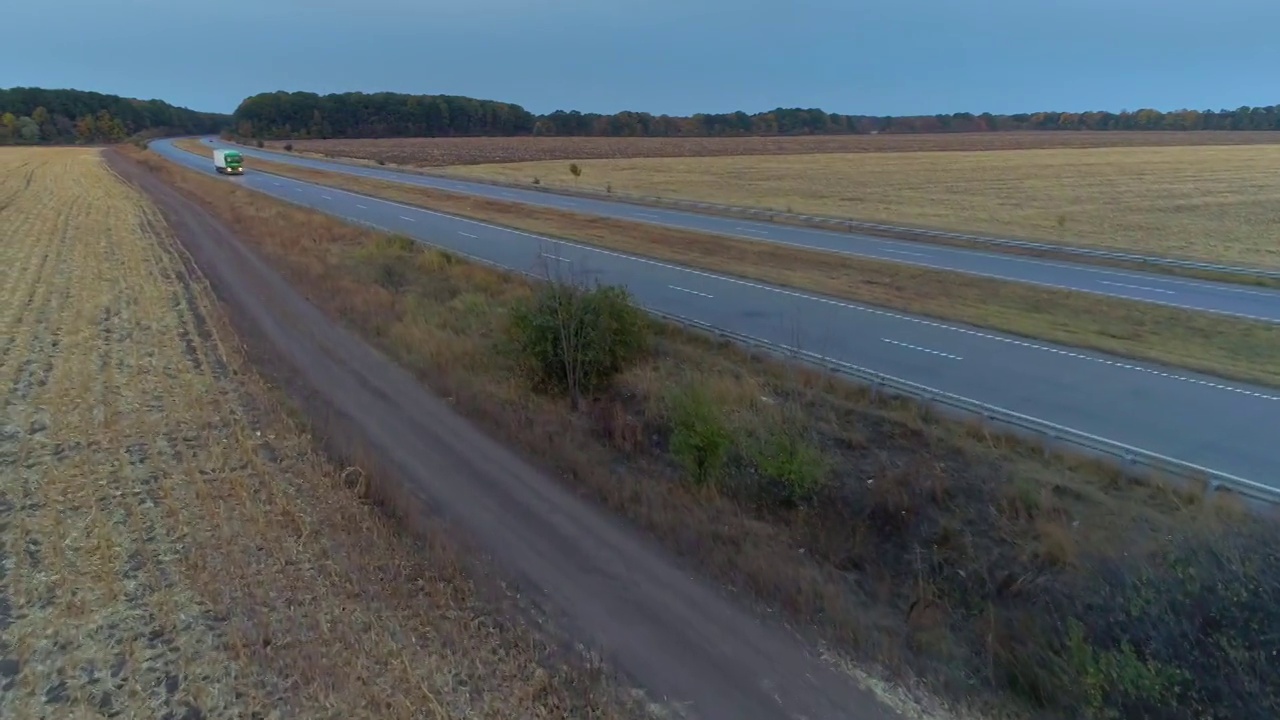 卡车行驶在一条笔直的道路上，在日落俯视图。日落时分，卡车在田野间的公路上行驶。视频素材