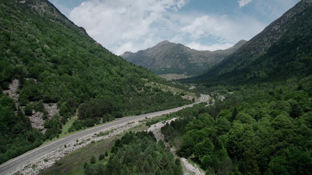 美丽的无人机视野的沥青公路在高山上。山脉消失在天空中，天空有些许阴云，但山峰被阳光照亮。视频素材