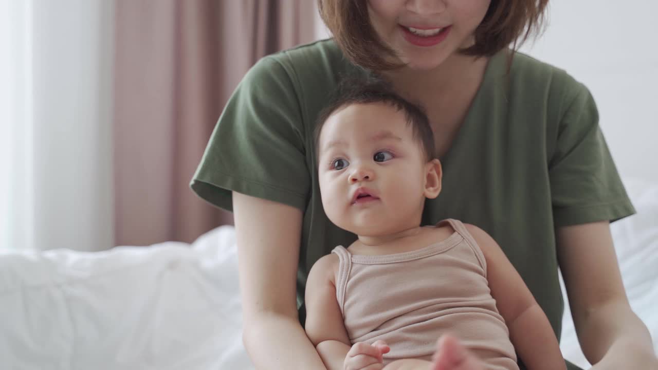 亚洲妇女母亲在卧室的床上玩婴儿婴儿蹒跚学步。天真宝贝与父母家庭关系良好。孩子在向妈妈学习的时候笑得很开心。视频素材