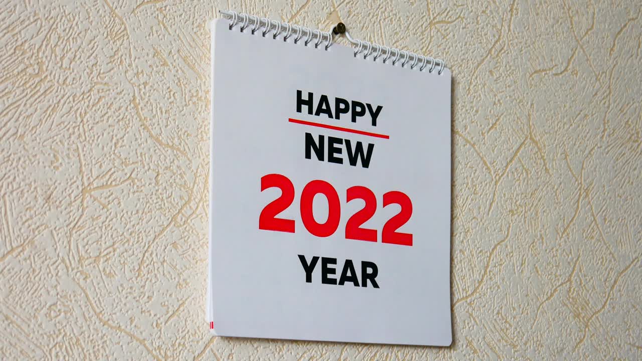 一个男人的手撕下挂在墙上的2022年日历扉页和1月页视频素材