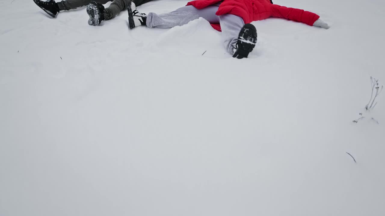 快乐的男人和女人堆雪天使。年轻的一家人躺在雪地里。视频素材