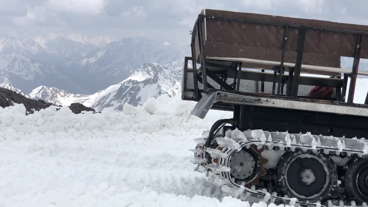 特写工作的宽雪地车骑在雪和耙子它的背景积雪覆盖的山。为滑雪季节和收获雪准备雪道的概念视频素材