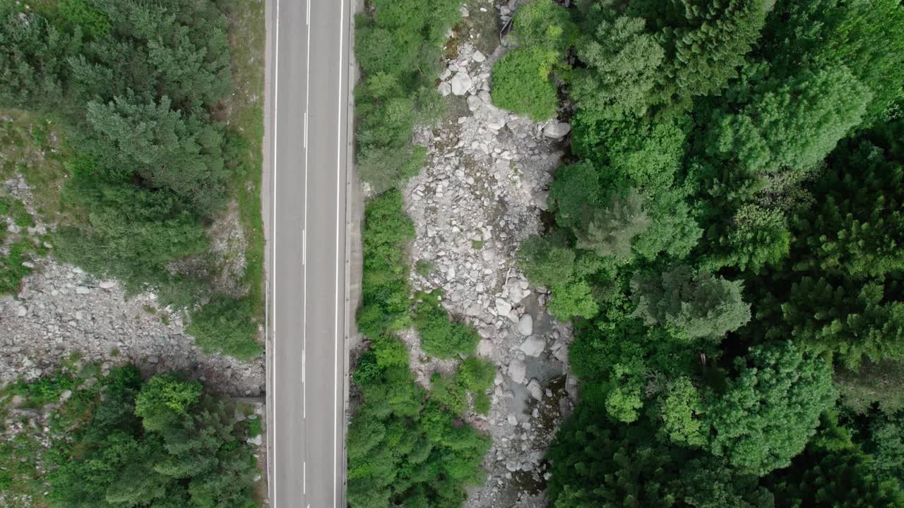 柏油路在一个山谷的高山。在它旁边，一条山间河流在树木之间蜿蜒流过。视频素材