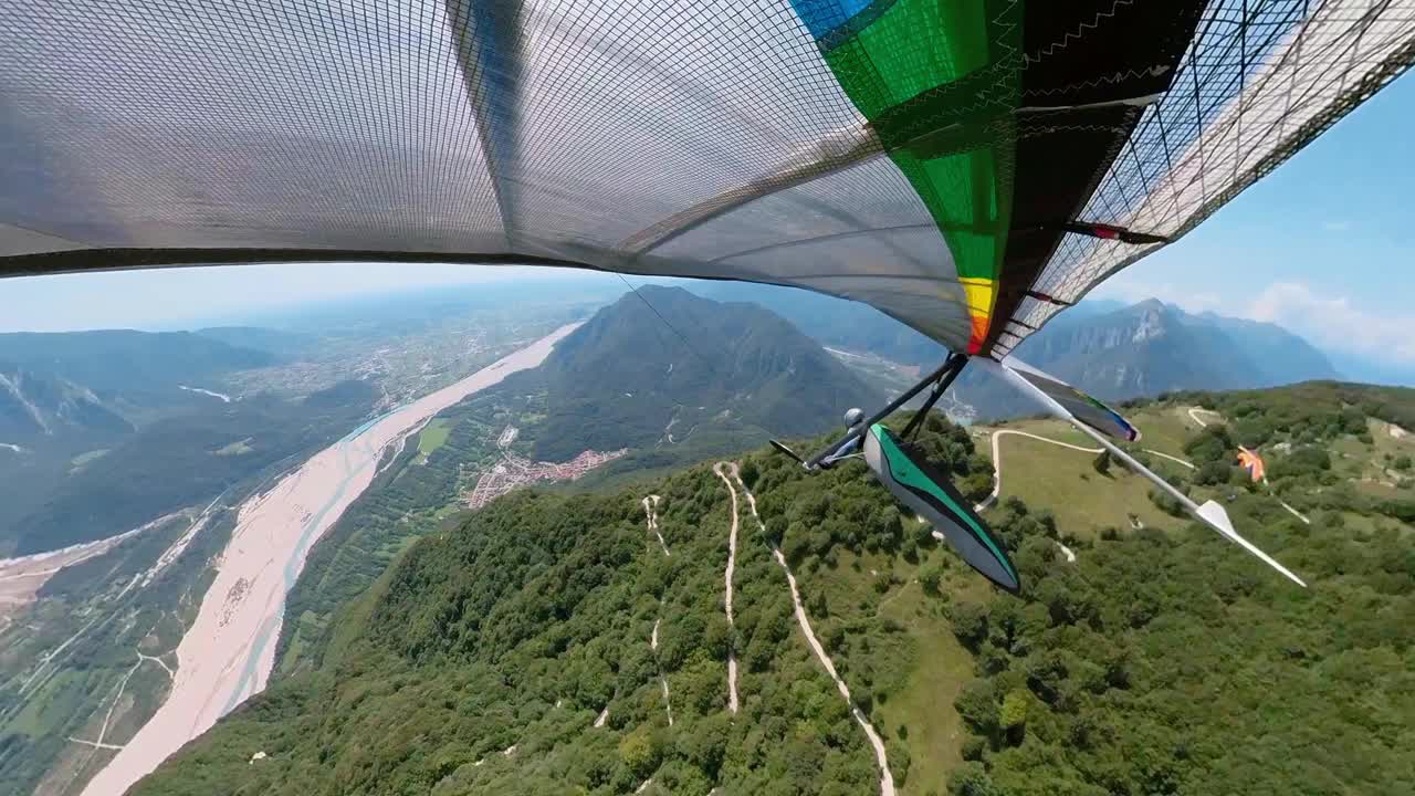 悬挂式滑翔机在蜿蜒道路上方的山谷中翱翔视频素材