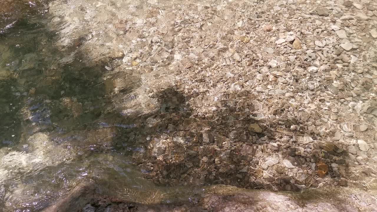 一个明确的河。一个年轻人涉水越过寒冷的山涧。视频素材