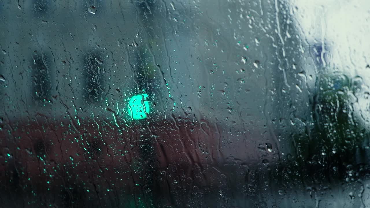 雨点落在窗户与散景光的效果。大雨中车内行驶，模糊了红绿灯的背景。雨滴渗透视频素材