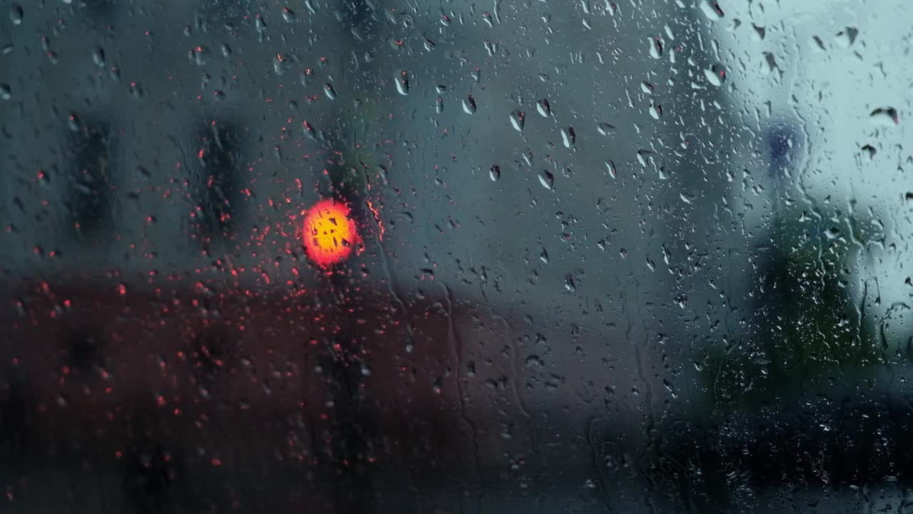 雨点落在窗户与散景光的效果。大雨中车内行驶，模糊了红绿灯的背景。雨滴渗透视频素材