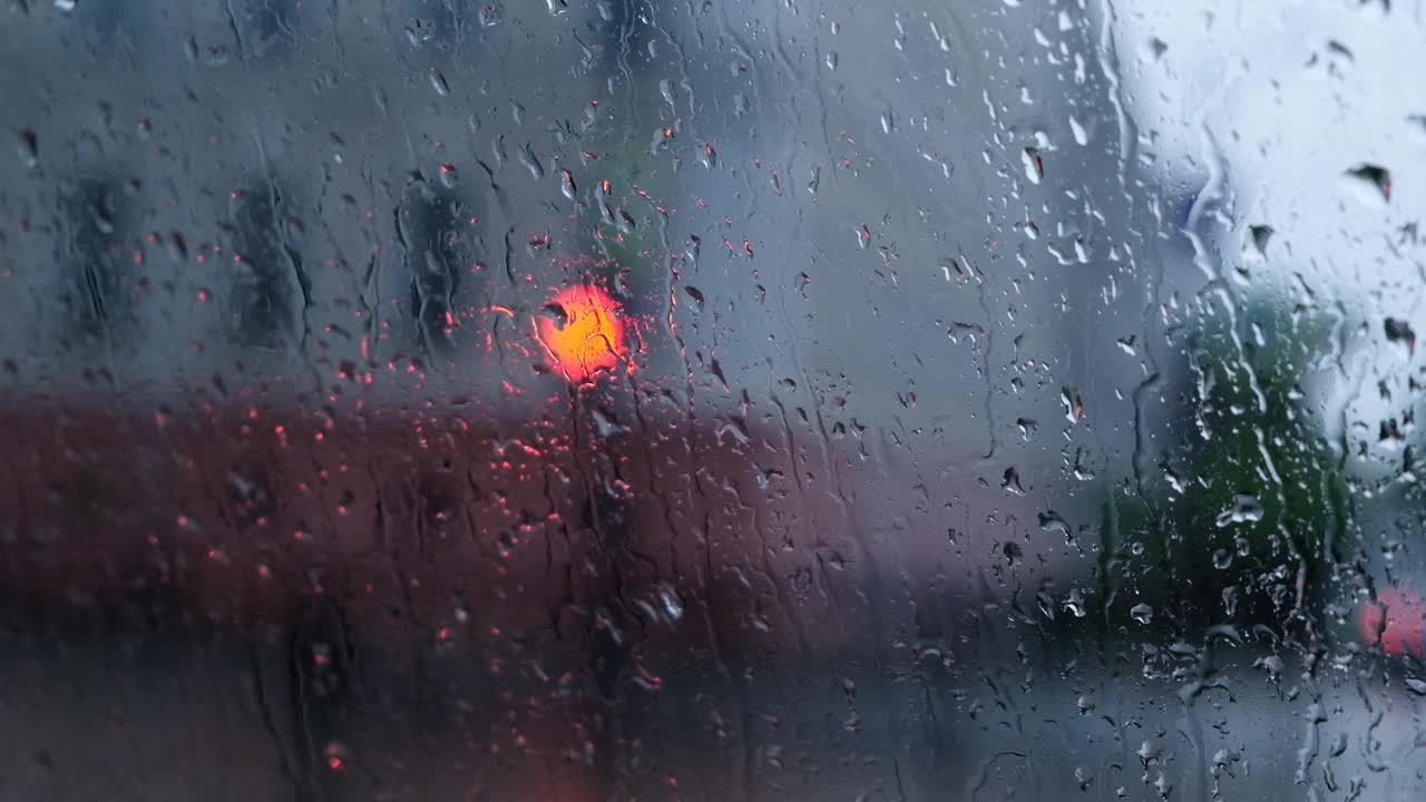 雨点落在窗户与散景光的效果。大雨中车内行驶，模糊了红绿灯的背景。雨滴渗透视频素材